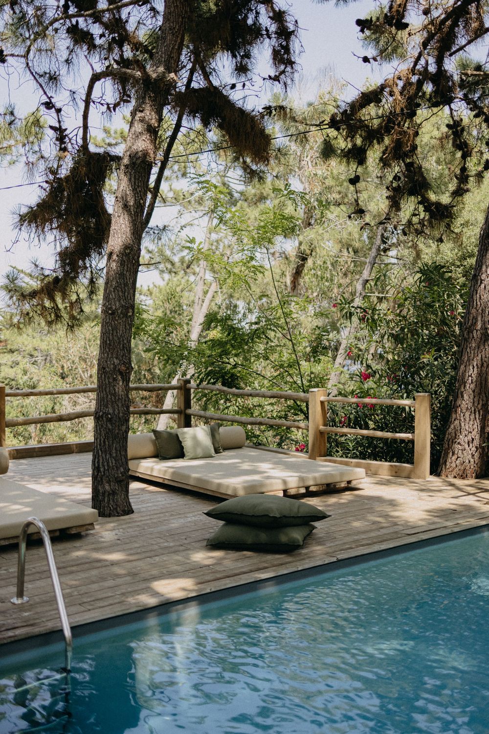Luxurious wooden deck with lounge chairs and a swimming pool surrounded by tall pine trees in a tranquil setting.