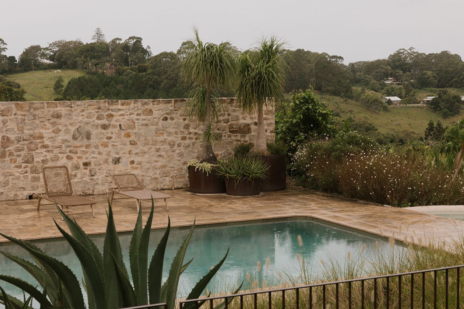 Scenic countryside property with stone walls, palm trees, and a swimming pool surrounded by lush landscaping.