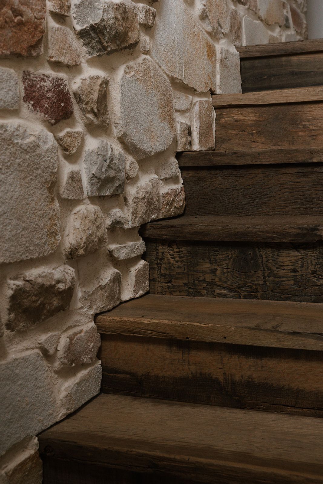 Old wooden stairs with rough stone wall texture create a rustic architectural detail in a historic building.