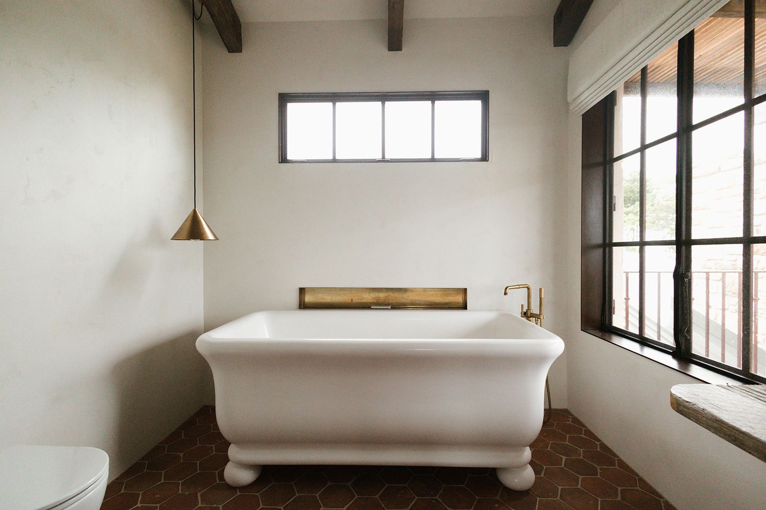 Minimalist white bathroom interior with exposed wooden beams and large windows letting in natural light.