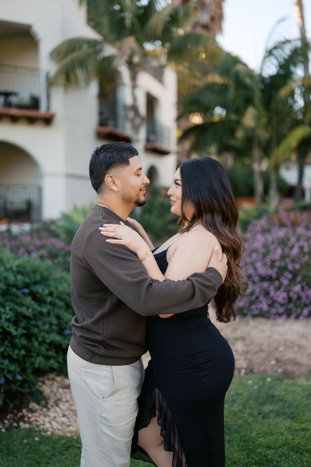 A romantic moment captured between a couple dancing on grass with Mediterranean architecture behind them.