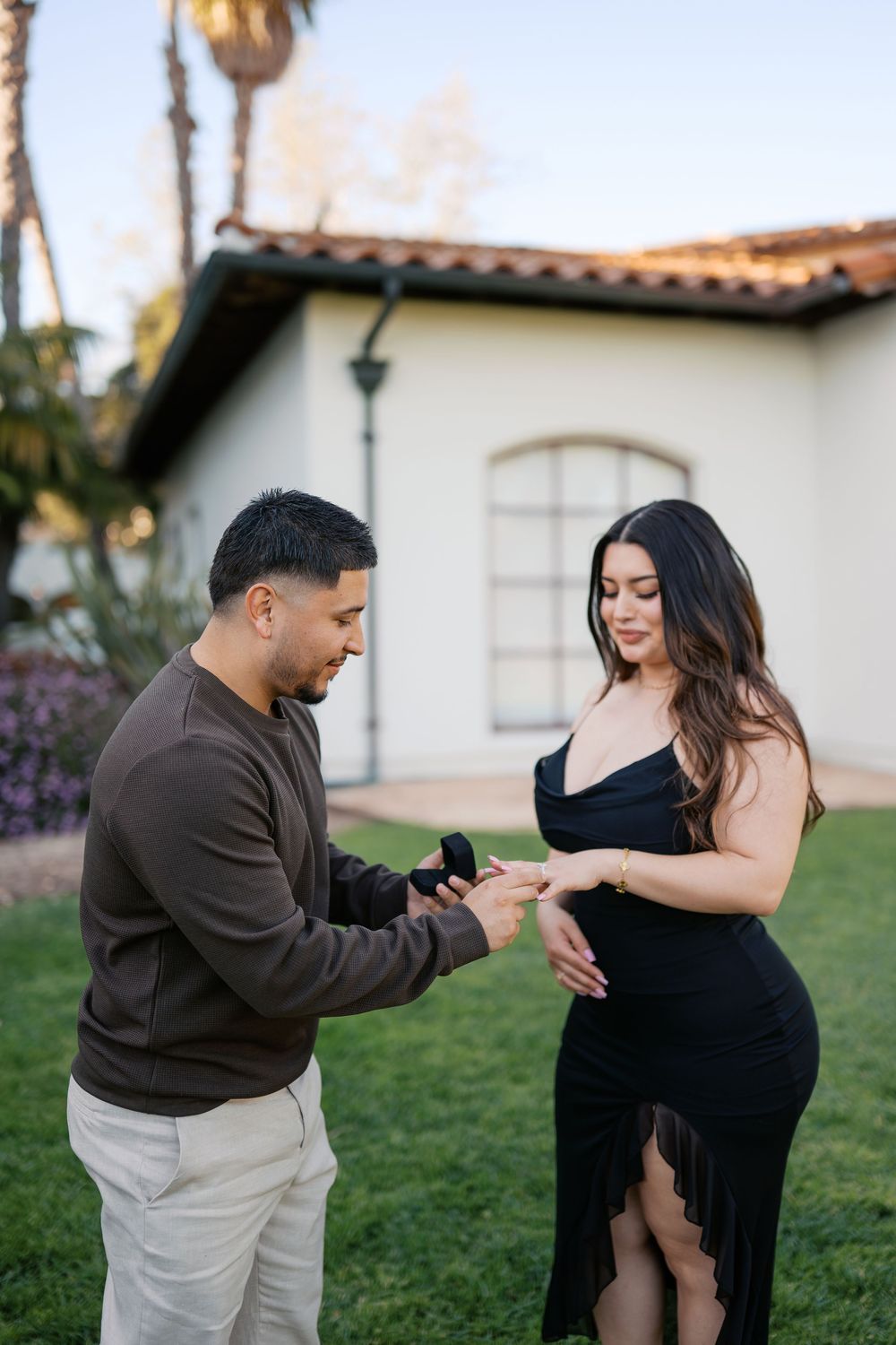 A couple shares a tender moment dancing together on a grassy lawn with Spanish-style architecture in the background.