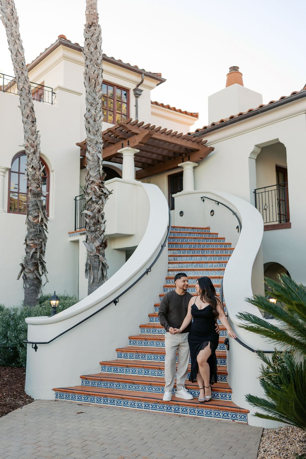 A couple sits together on decorative Spanish tile stairs with white stucco walls and palm trees.