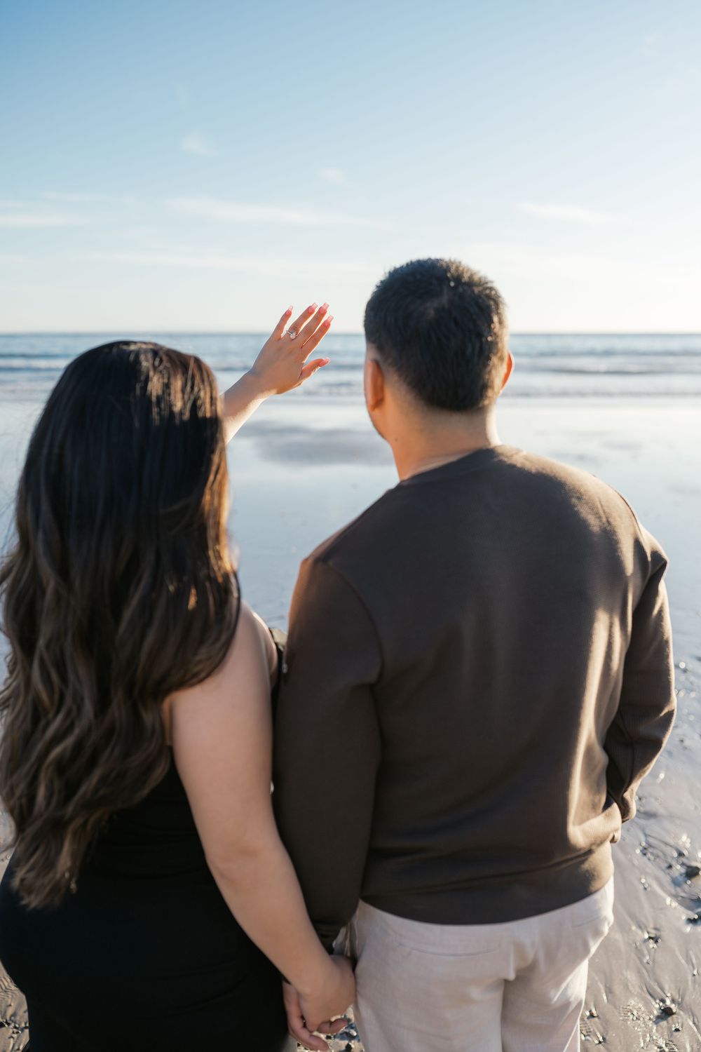 Couple walking together on a scenic beach at sunset with ocean waves in the background.