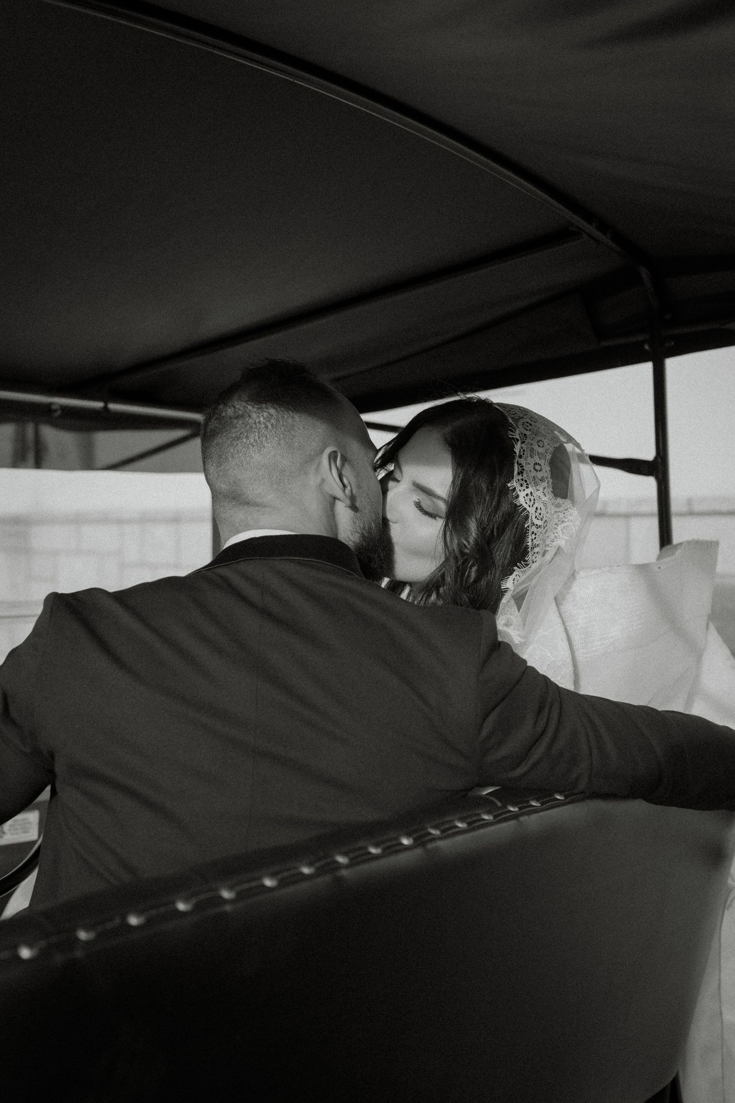 Black and white close-up detail of a bride and groom's formal wedding attire showing lace dress and tuxedo.