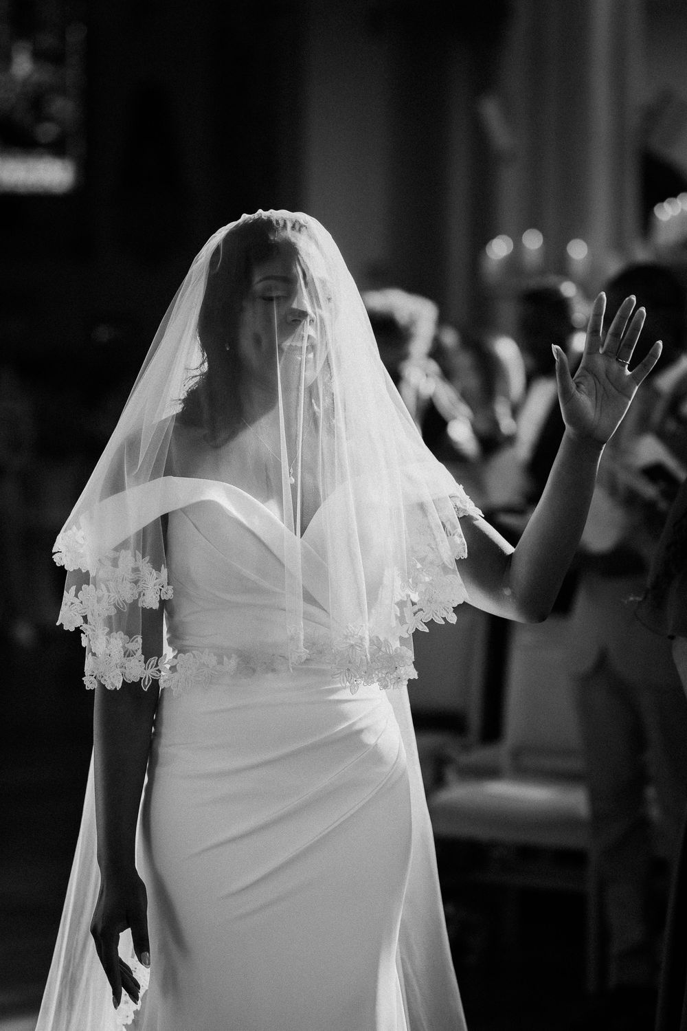 A bride in a white wedding dress with a delicate veil stands silhouetted against a dark background.