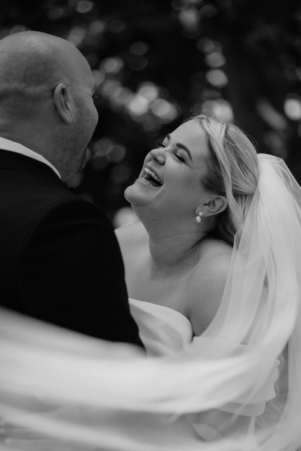 Black and white sequence of a bride in a flowing veil laughing joyfully during an outdoor wedding photoshoot.