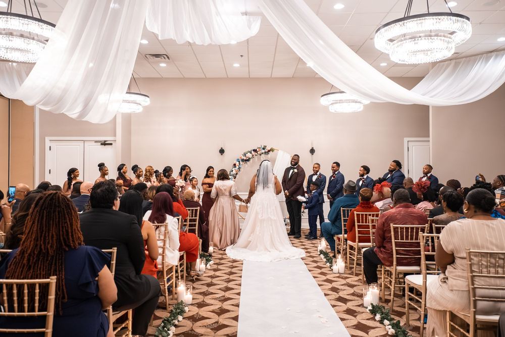 Wedding ceremony in an elegant ballroom with white draping and chandeliers as guests look on at Carollwood Country Club in Tampa, Florida