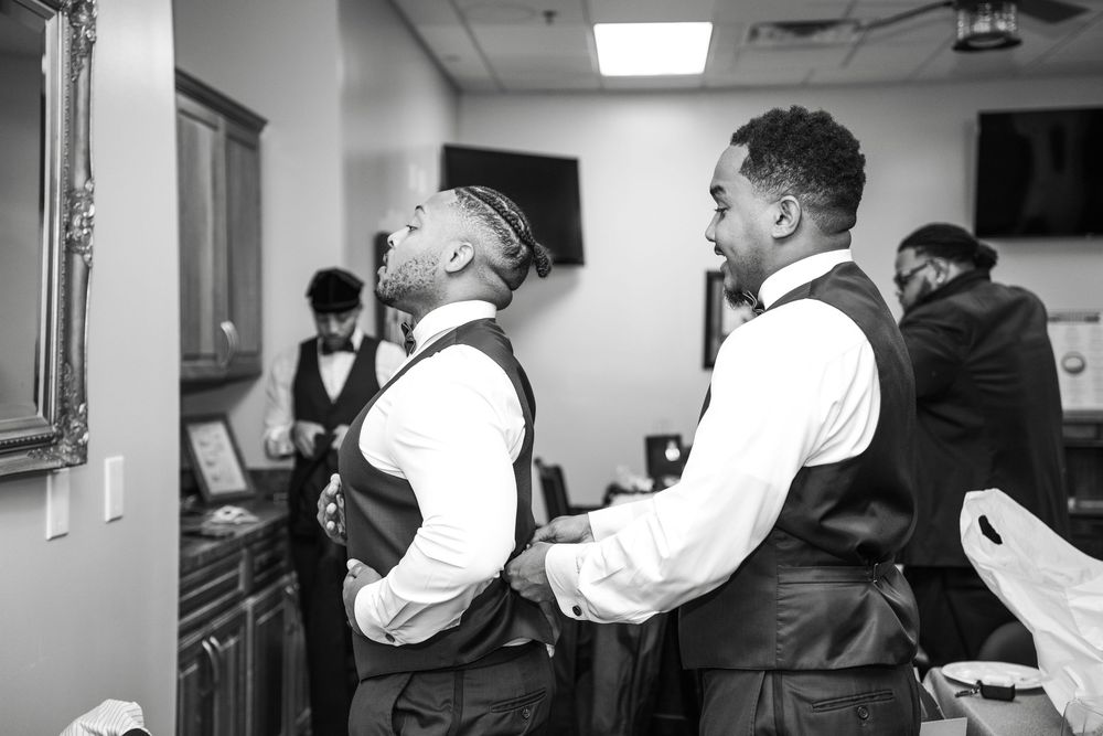 Two people in formal white dress shirts and vests stand together in what appears to be a preparation room at Carollwood Country Club in Tamp