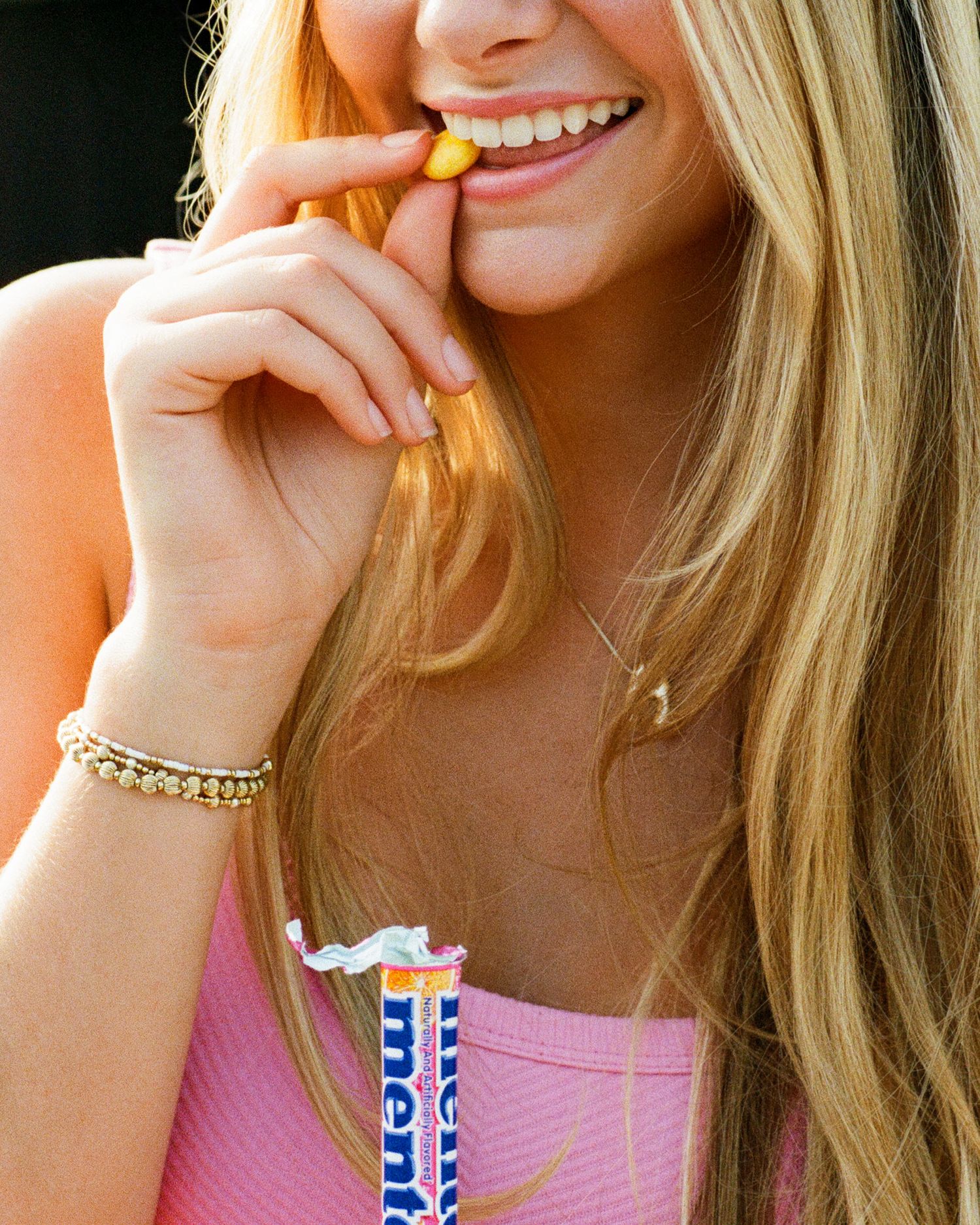 A person in a pink top snacking on mentos candies with a happy expression.