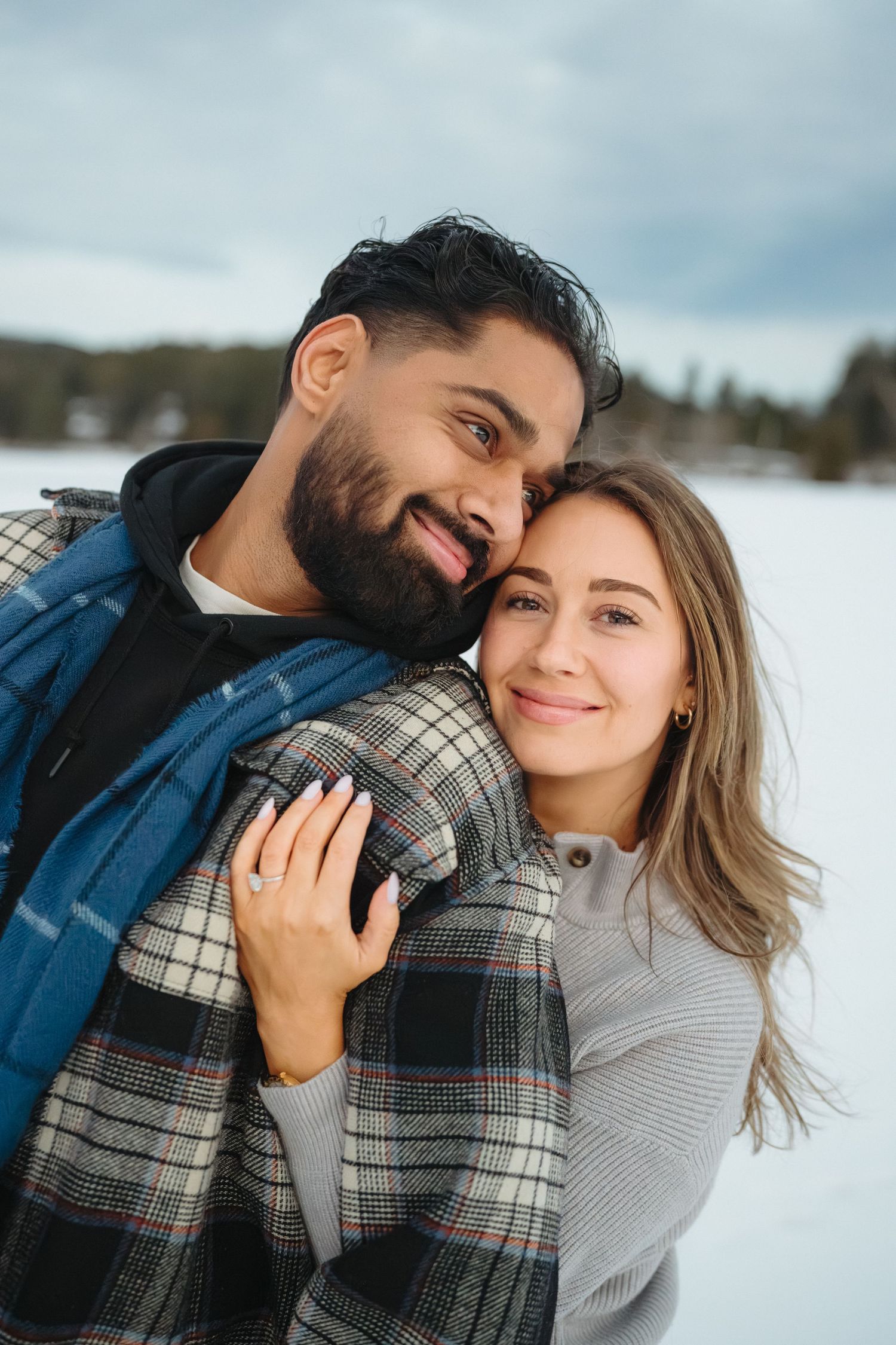 Romantic winter photoshoot with a couple cuddling in warm sweaters against a snowy mountain backdrop.