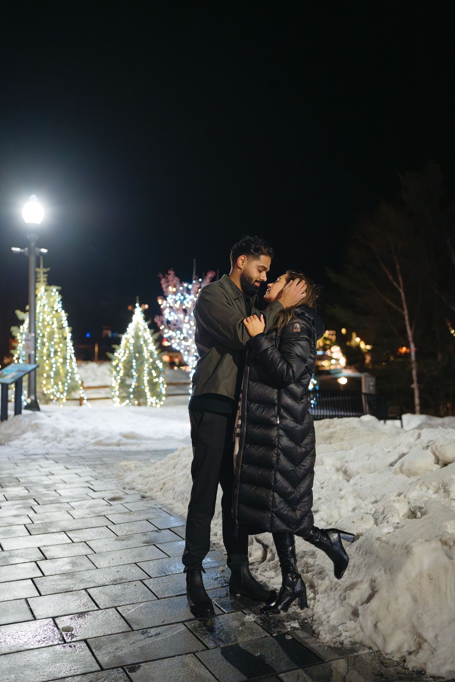 Illuminated Christmas trees and decorative lights create a magical winter scene in the snow at night.