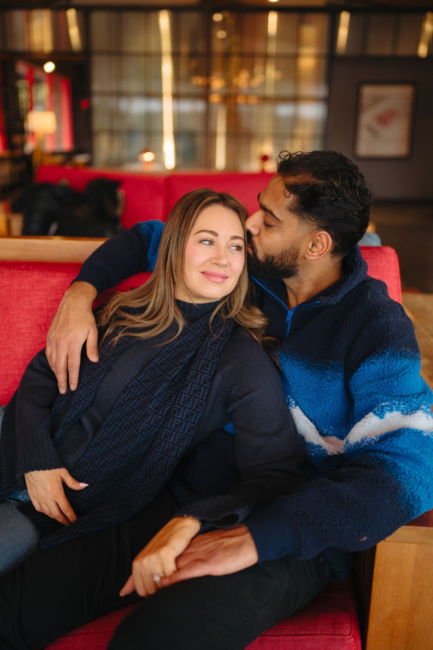 Couple cuddling and relaxing together on a red couch in a cozy indoor setting.