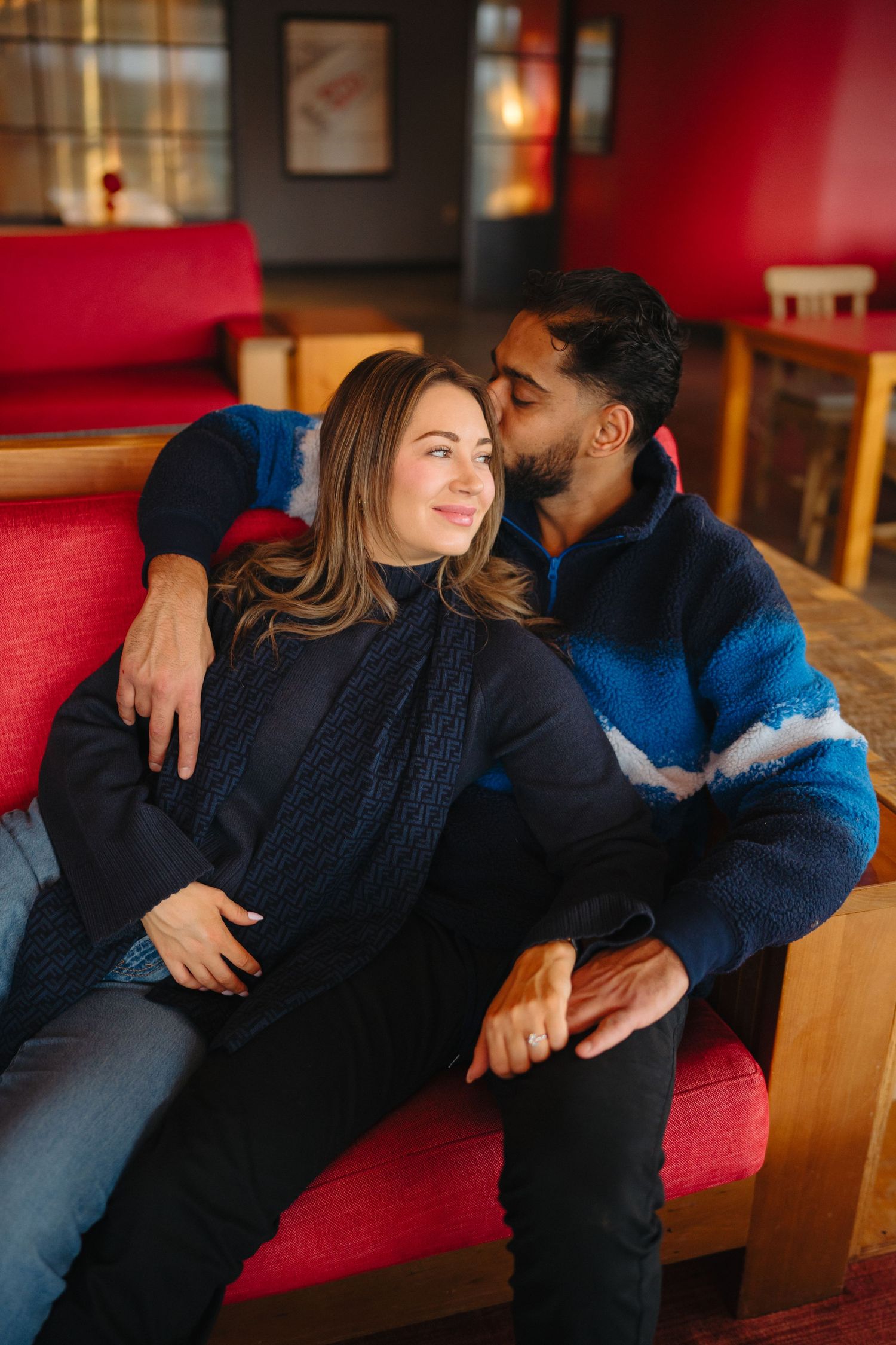Cozy indoor photoshoot on a red couch showing tender romantic moments.