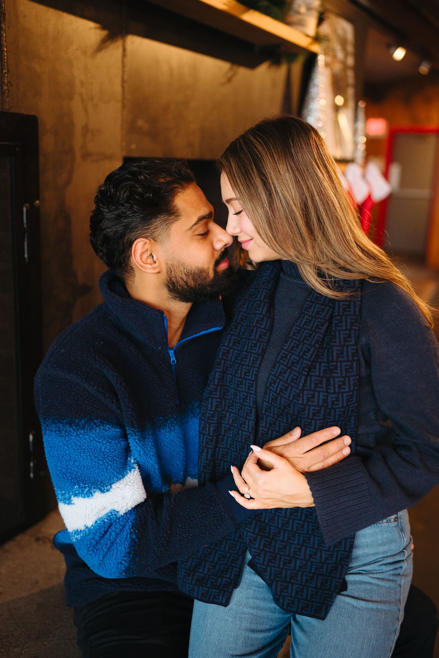 A couple in navy blue outfits share an intimate moment in a dimly lit hallway.