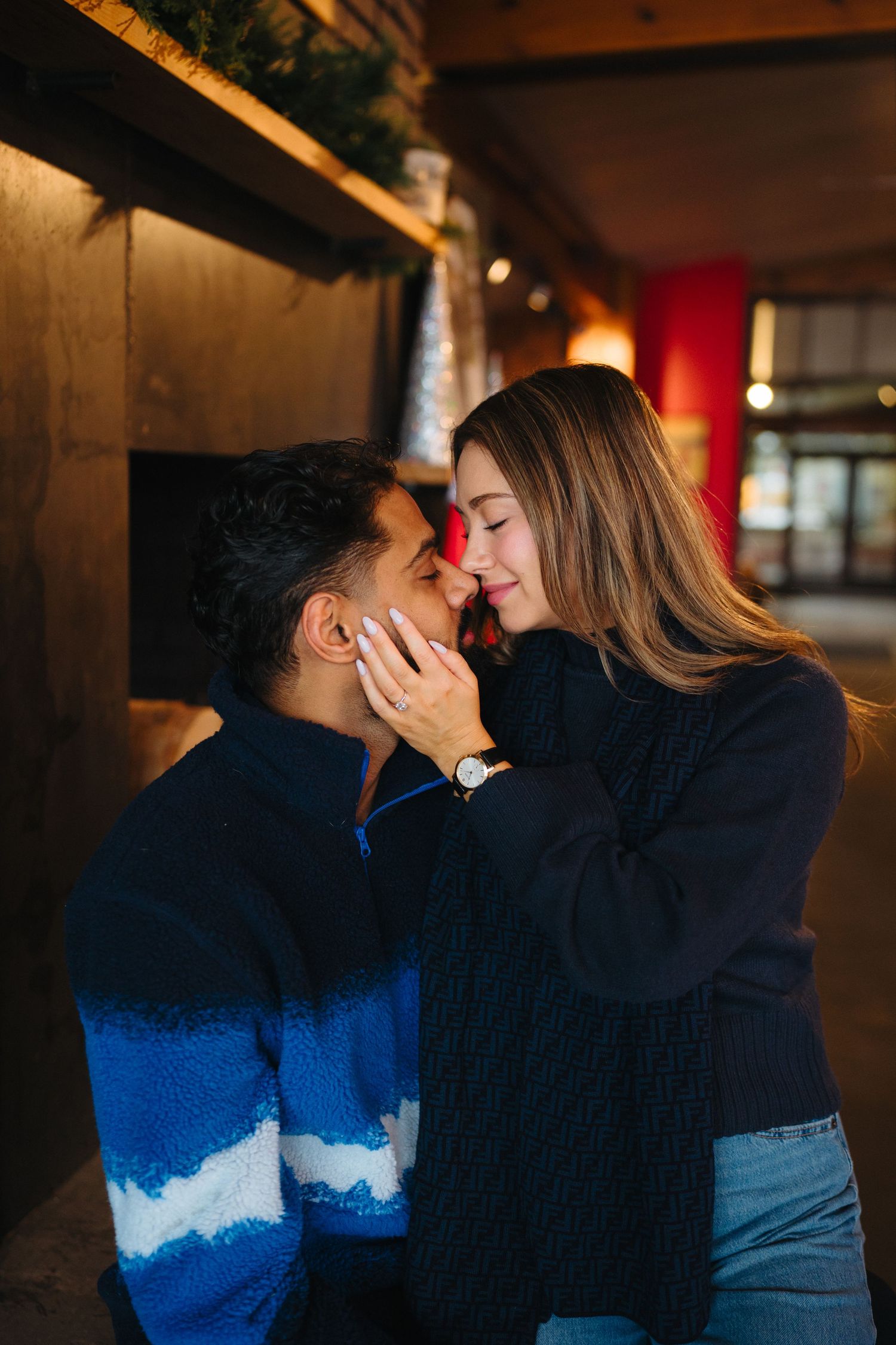 A couple in blue and black outfits share an intimate kiss in a dimly lit indoor setting.