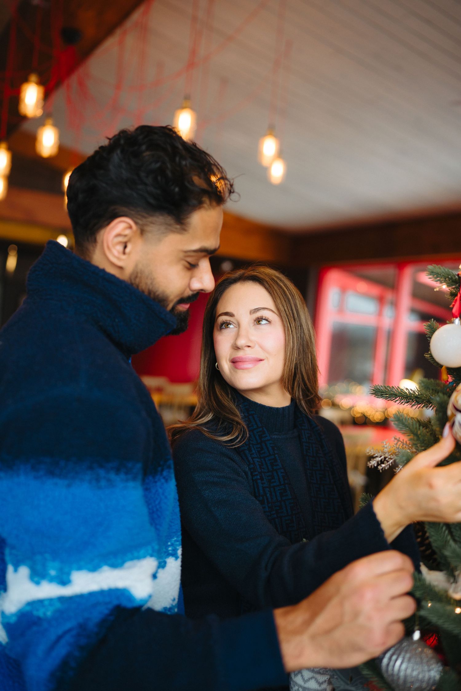 Couple decorating for the holidays together with twinkling lights and ornaments in a warm indoor setting.