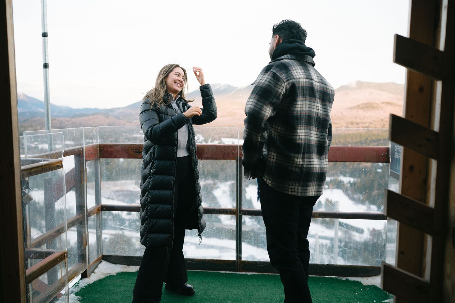 Two people enjoying a scenic mountain view from an observation deck on a winter day.