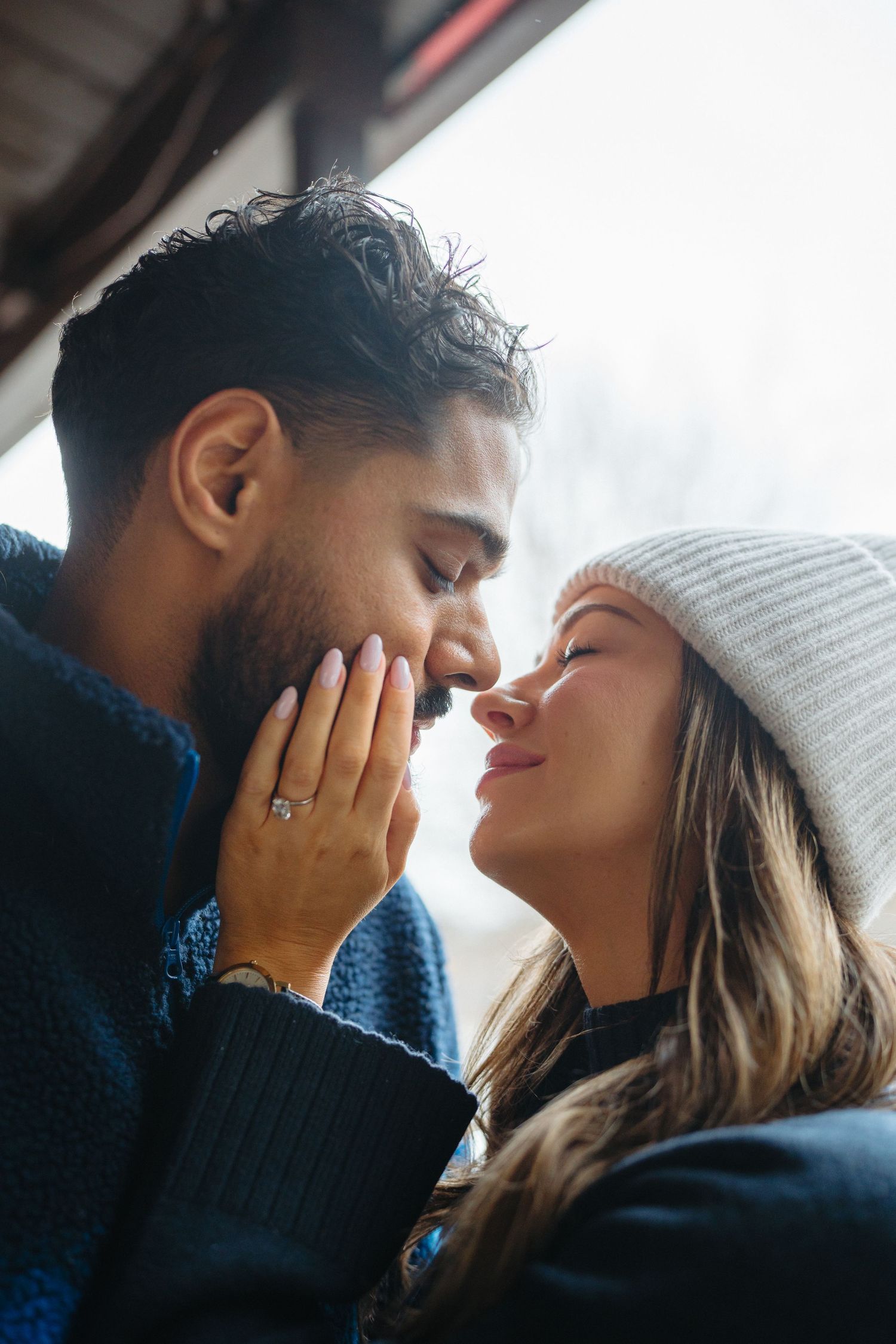 A romantic close-up moment between two people in winter attire with soft natural lighting.