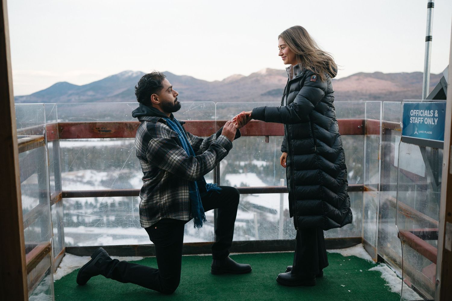 Couple sharing a special moment on an outdoor viewing platform with mountain scenery.