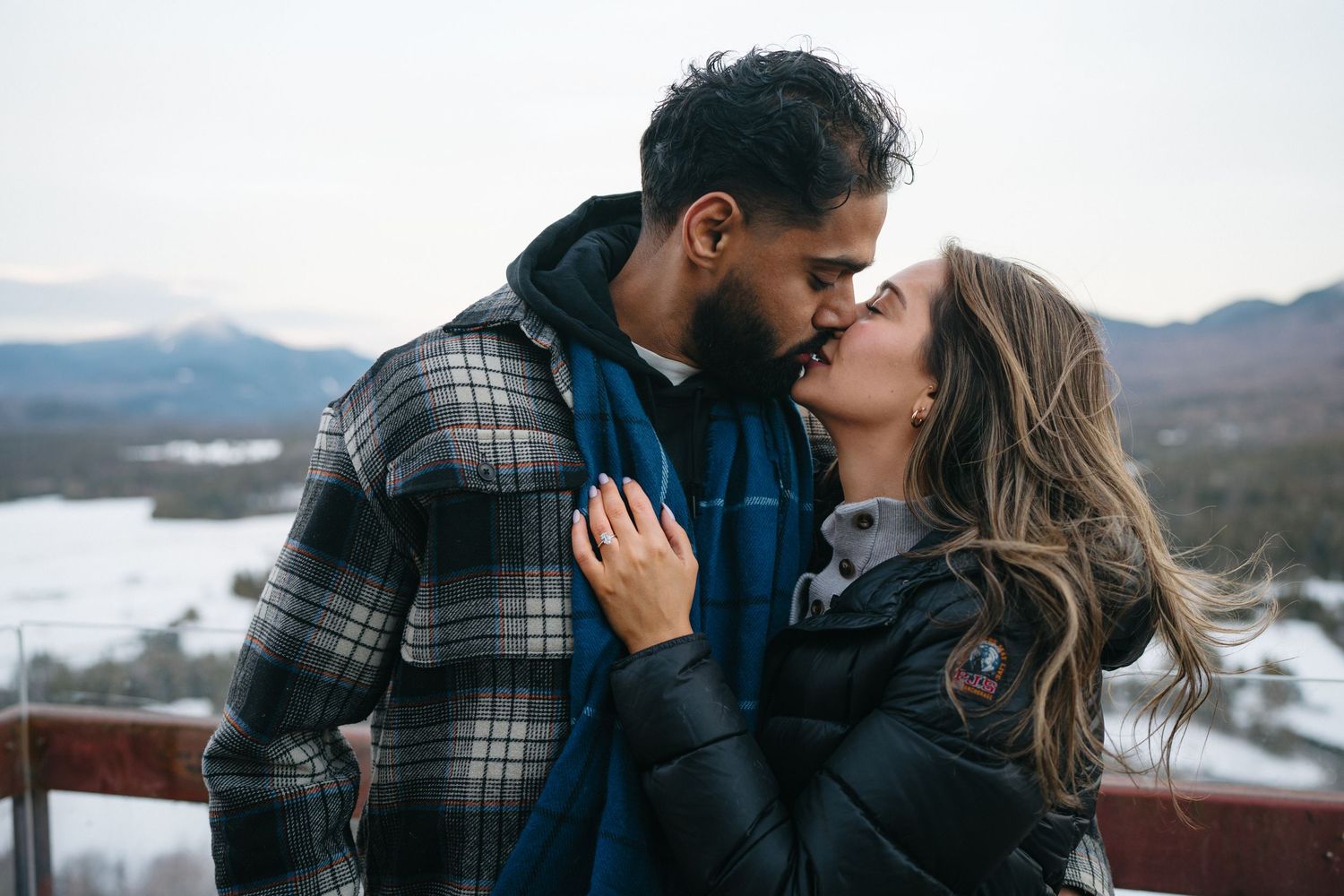Romantic moment shared between couple on observation deck with snowy mountains in background.