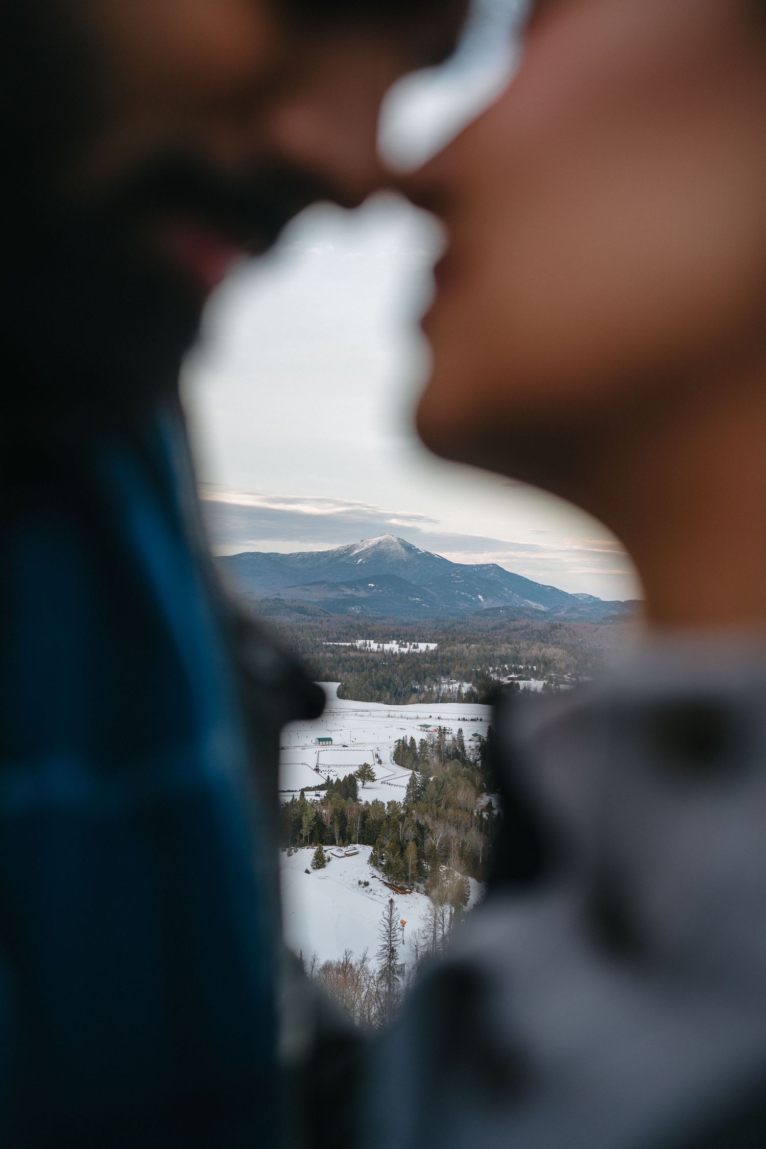 Snow-covered mountain landscape viewed through a silhouetted frame with distant peaks and valleys.