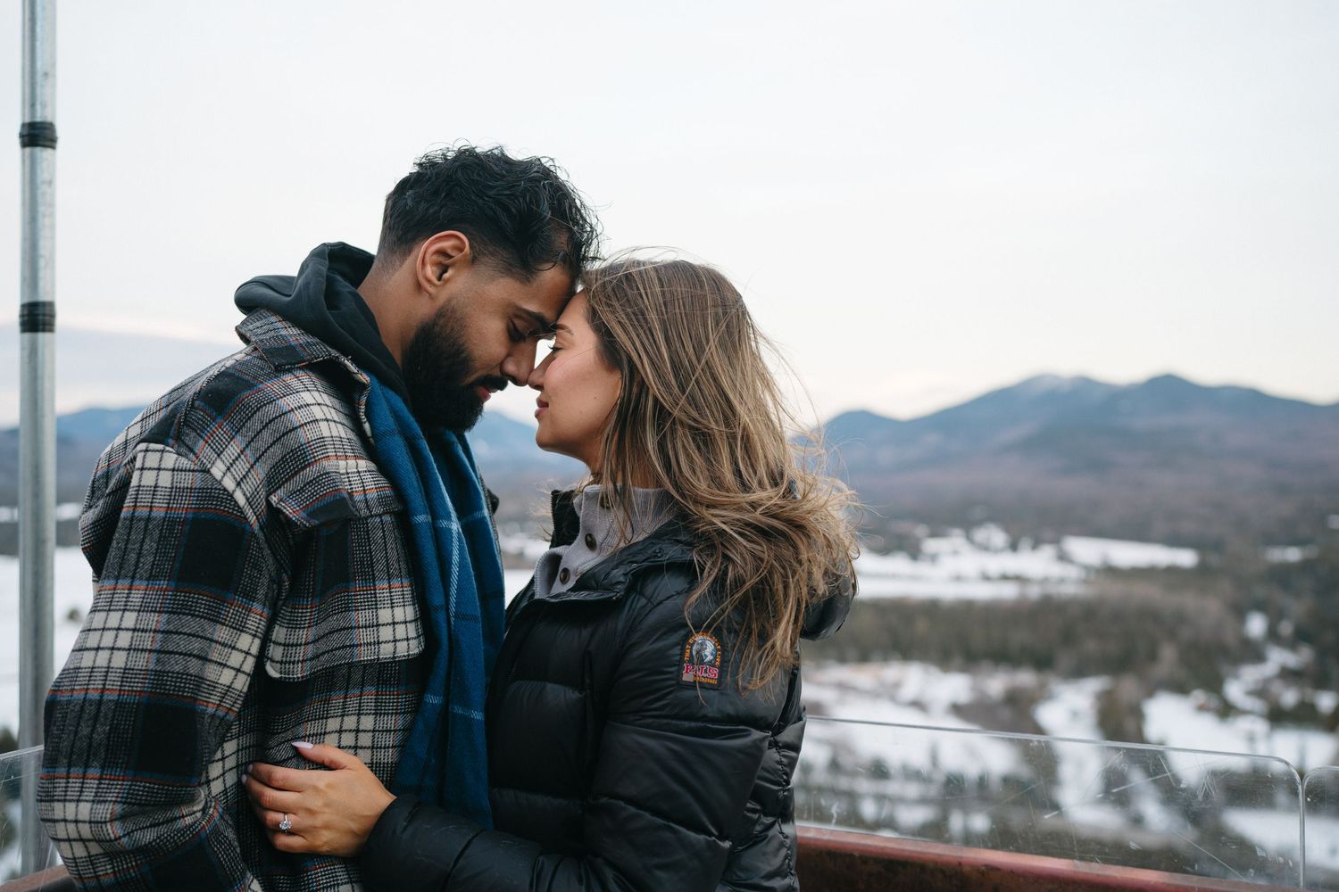 Intimate moment between couple on mountain viewing platform during winter.