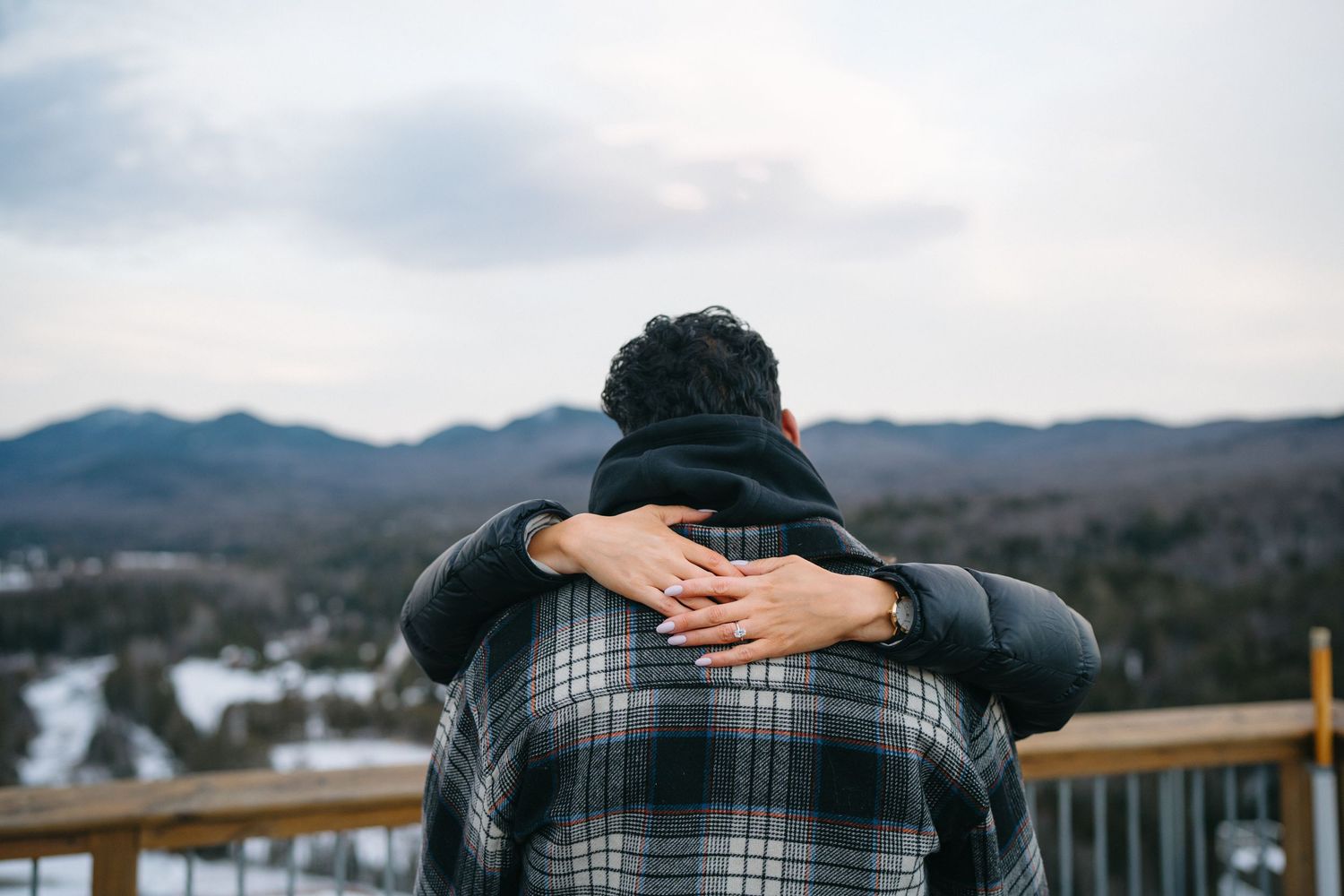 Two people embracing on a wooden deck overlooking snowy mountain vistas.