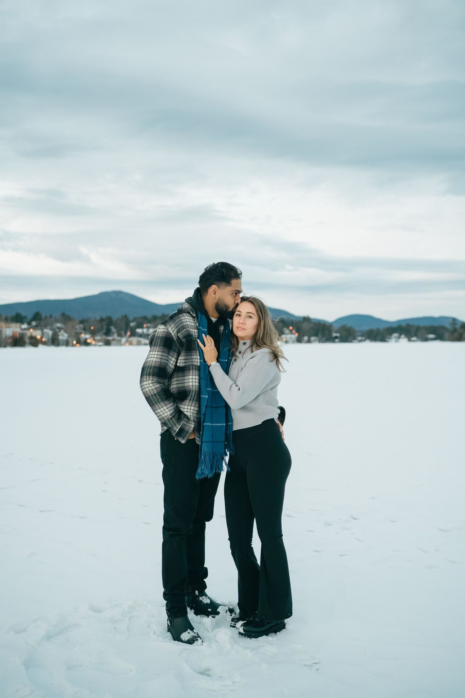 Couple sharing an intimate moment in a snow-covered landscape with mountains in the distance.