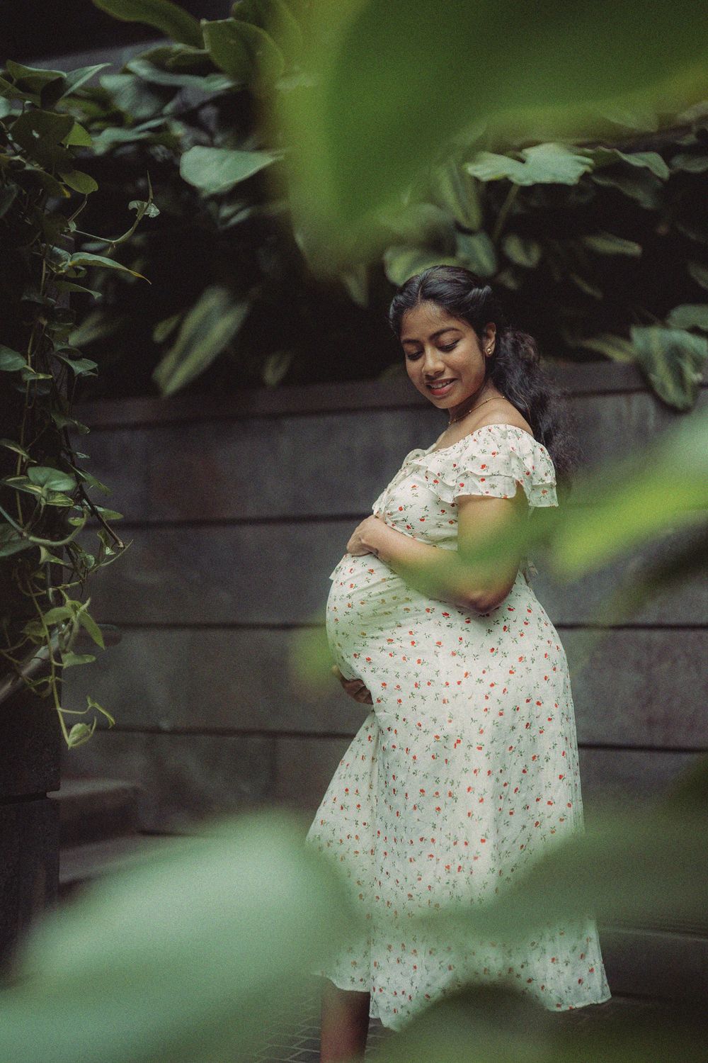 Maternity photo of person in floral dress posing in garden setting.