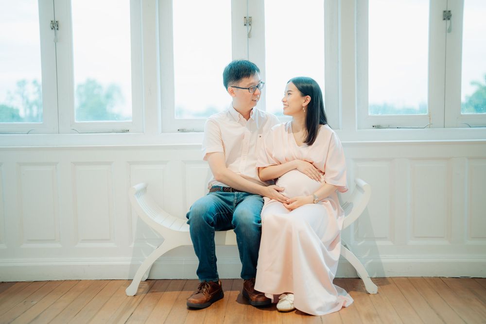 Couple sitting in white chairs by large windows in bright minimal interior setting.