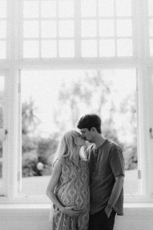 A romantic black and white silhouette of an expectant couple sharing an intimate moment by a window.
