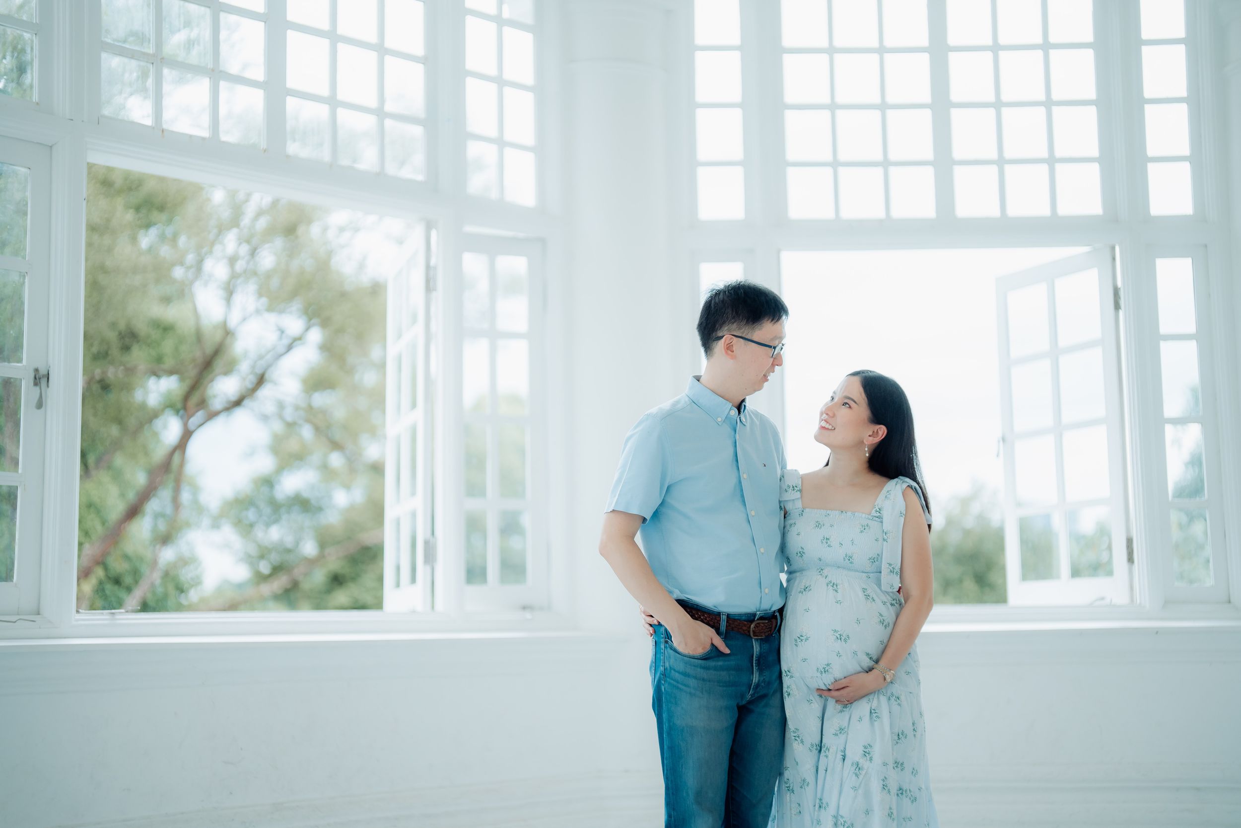 A couple shares a tender moment in a bright white room with large windows.