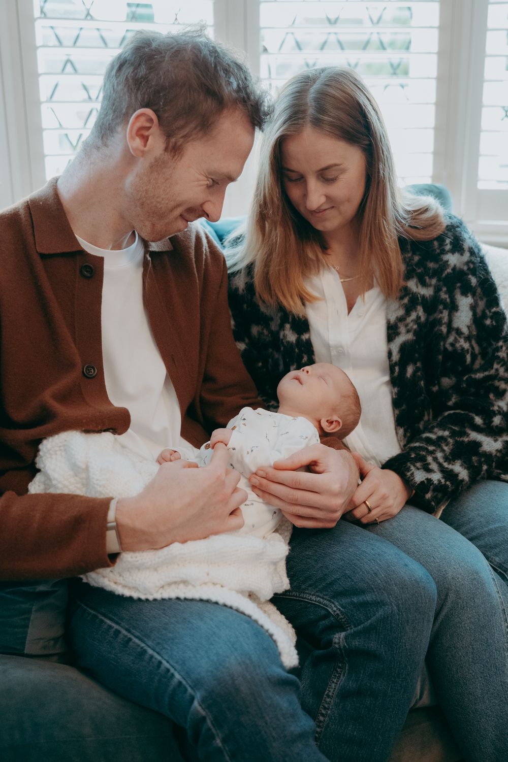 A couple shares tender moments with their baby in a series of candid photos by a window.