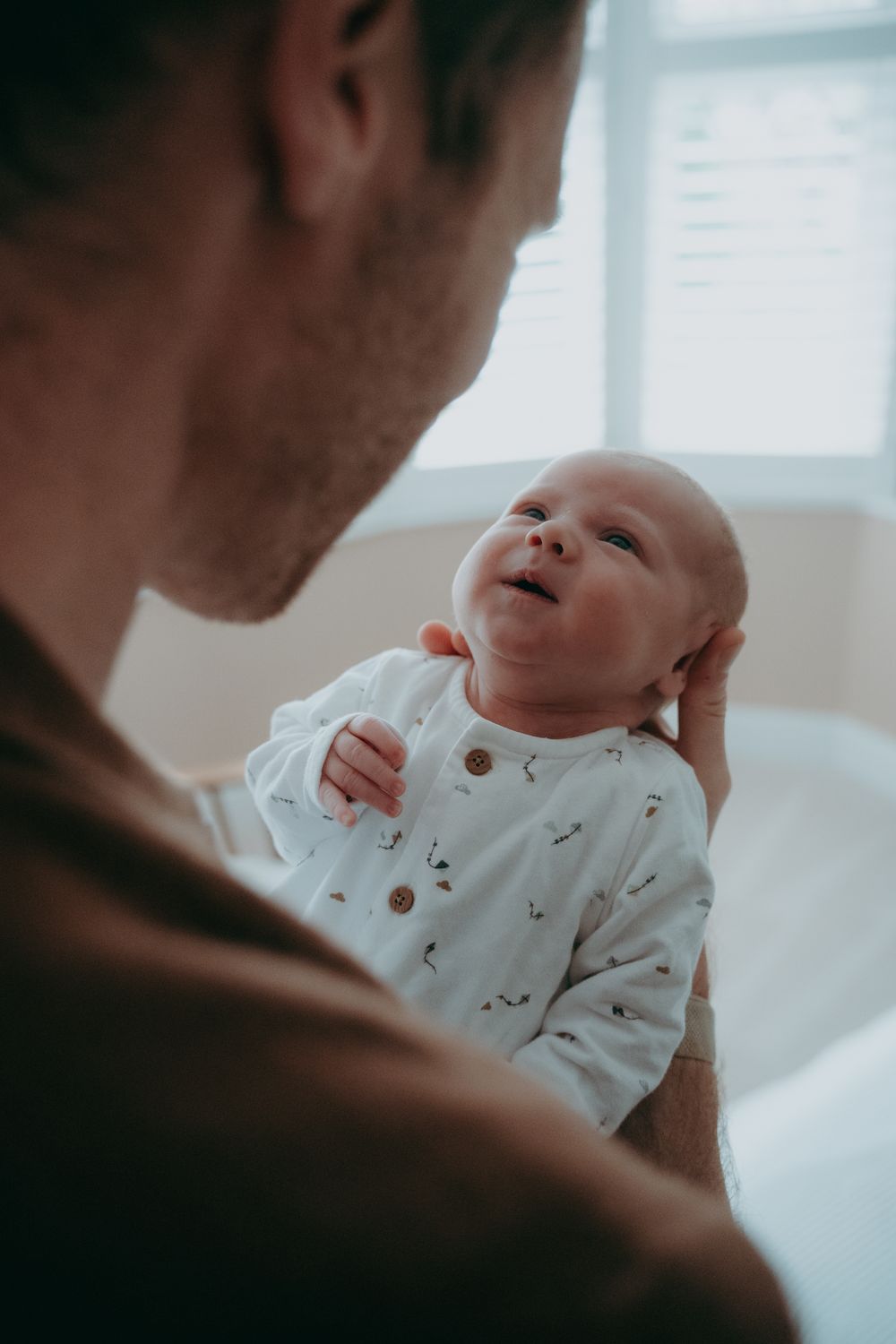 A tender moment between parent and baby wearing a white patterned onesie in soft natural lighting.