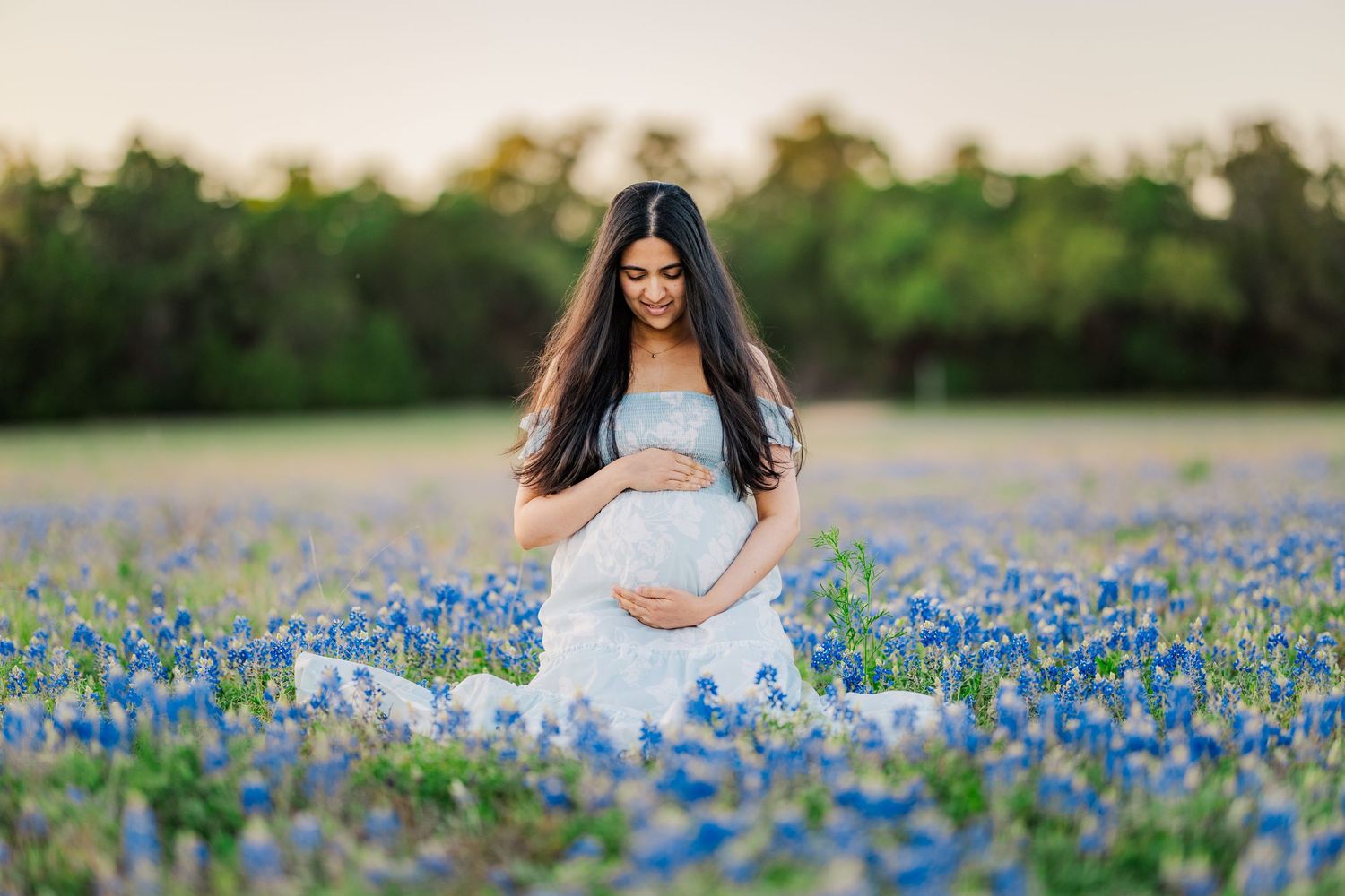 Expectant mother sitting in blooming bluebonnets during a Central Texas spring mini session with natural light photography.