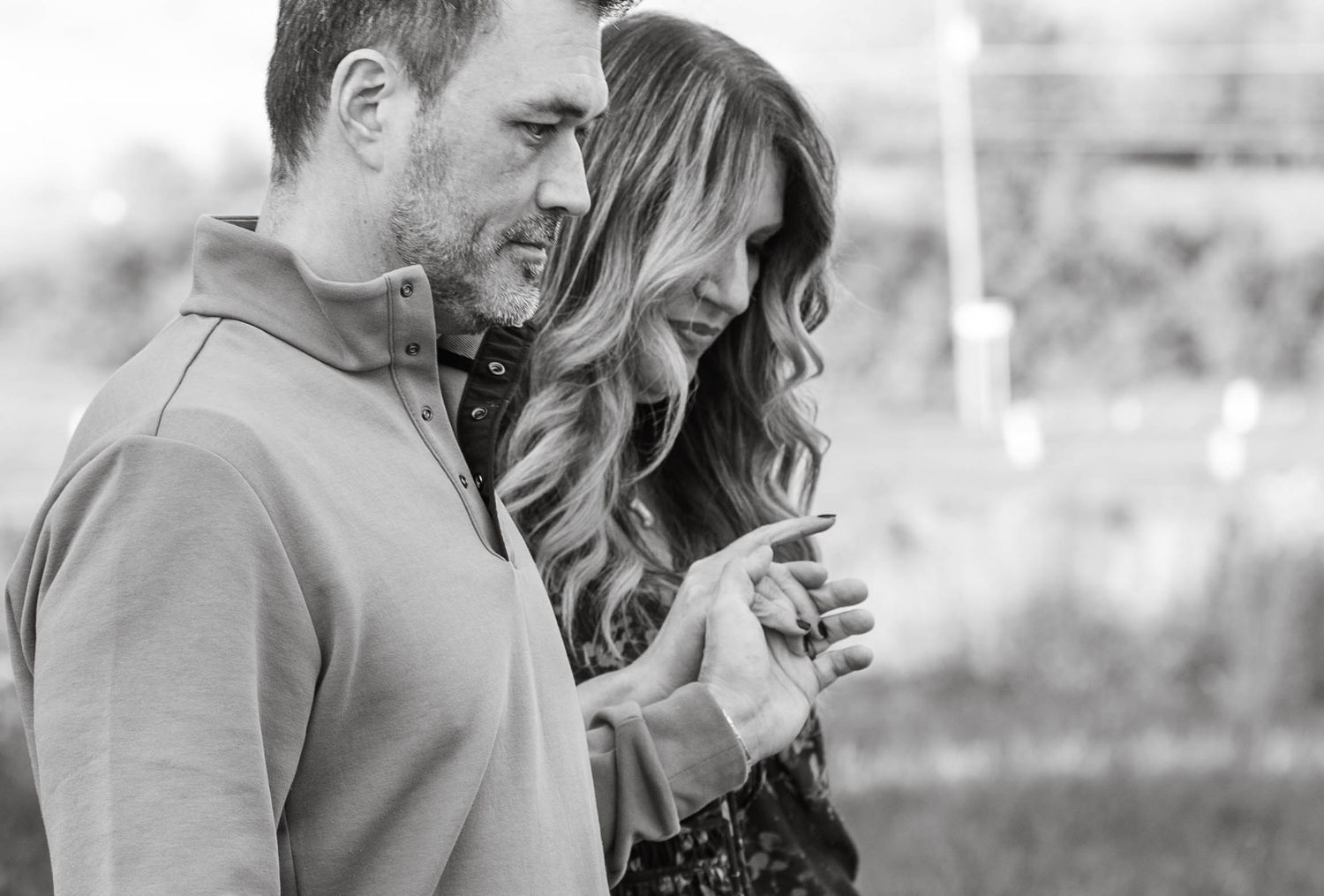 A couple shares an intimate black and white moment outdoors as they smile and lean in close together.