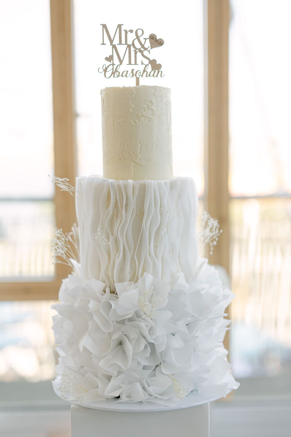 Elegant white wedding cake with ruffled details and a Mr & Mrs topper.