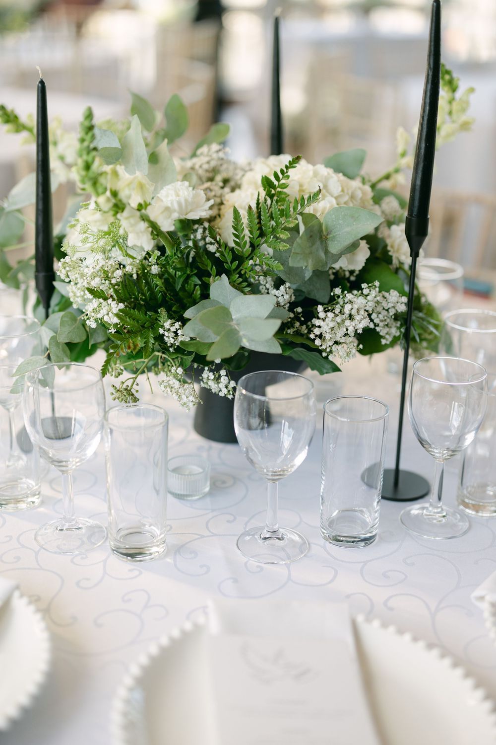 Elegant white floral centerpieces with greenery line a wedding reception table.