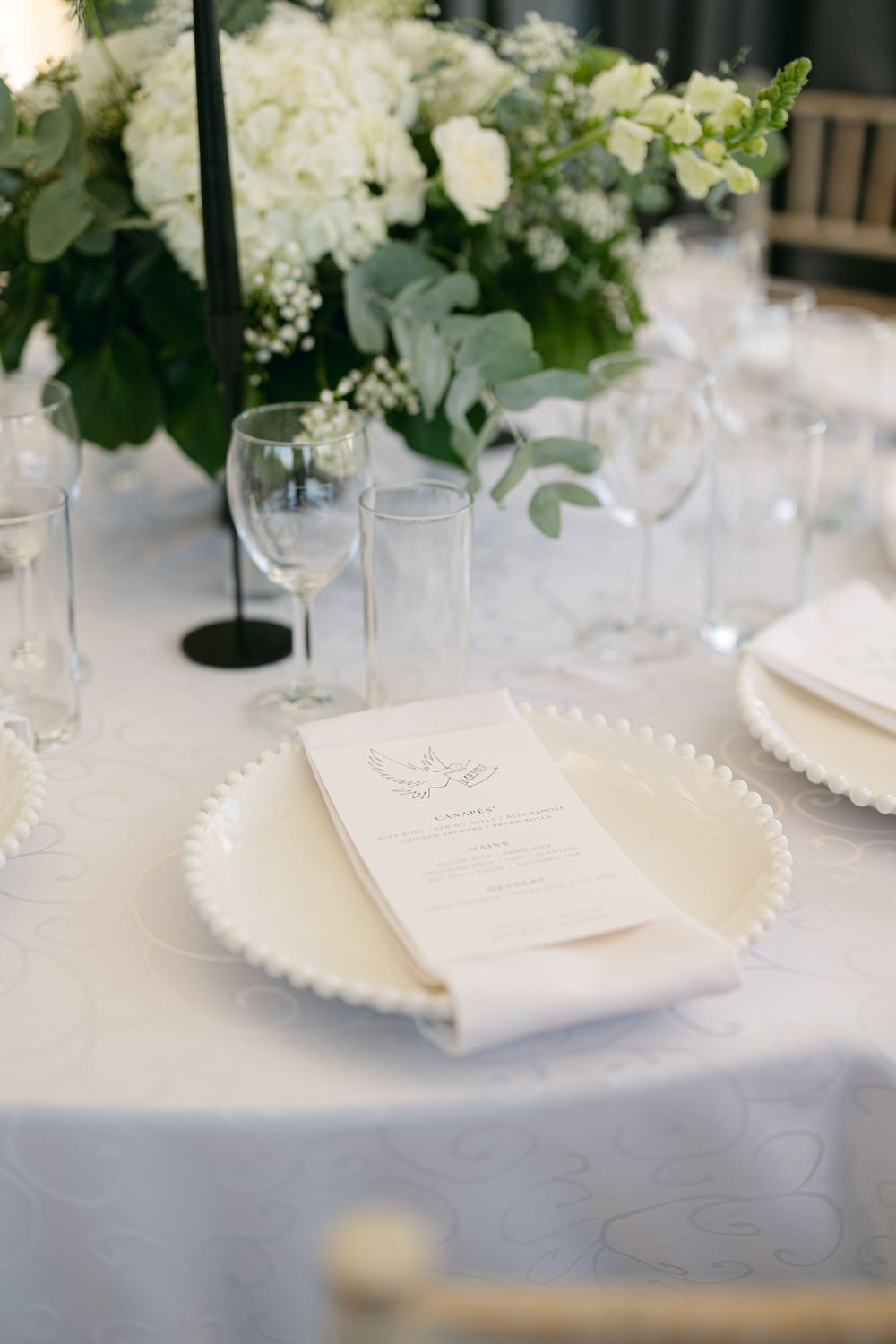 Elegant white floral centerpieces and place settings on tables at a formal wedding reception.