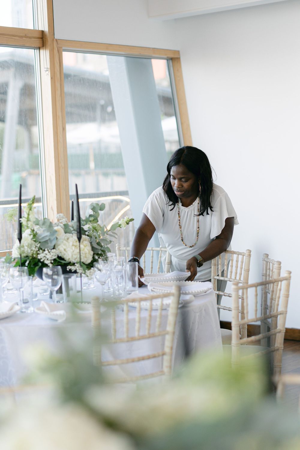 Wedding venue staff preparing elegant place settings with glassware and floral arrangements.