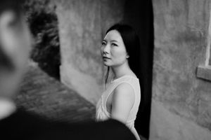Black and white artistic portrait of a woman in a white dress against a textured wall.