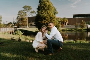 Couple sits together on grassy hill during golden hour sunset in romantic outdoor setting.