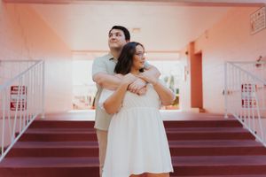 Couple in white outfits dancing and twirling together in a pink-tinted room during a romantic photoshoot.