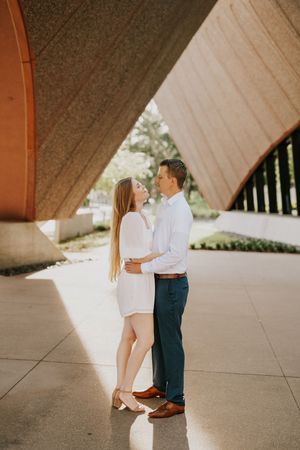 A couple shares an intimate moment under a modern architectural structure with dramatic lighting and shadows.