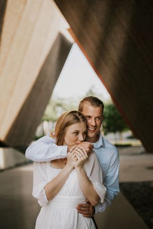 A couple shares an intimate moment under an angular concrete overhang with palm trees visible in the background.