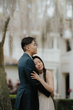 A couple shares an intimate moment outdoors against a soft, blurred winter background with bare trees.