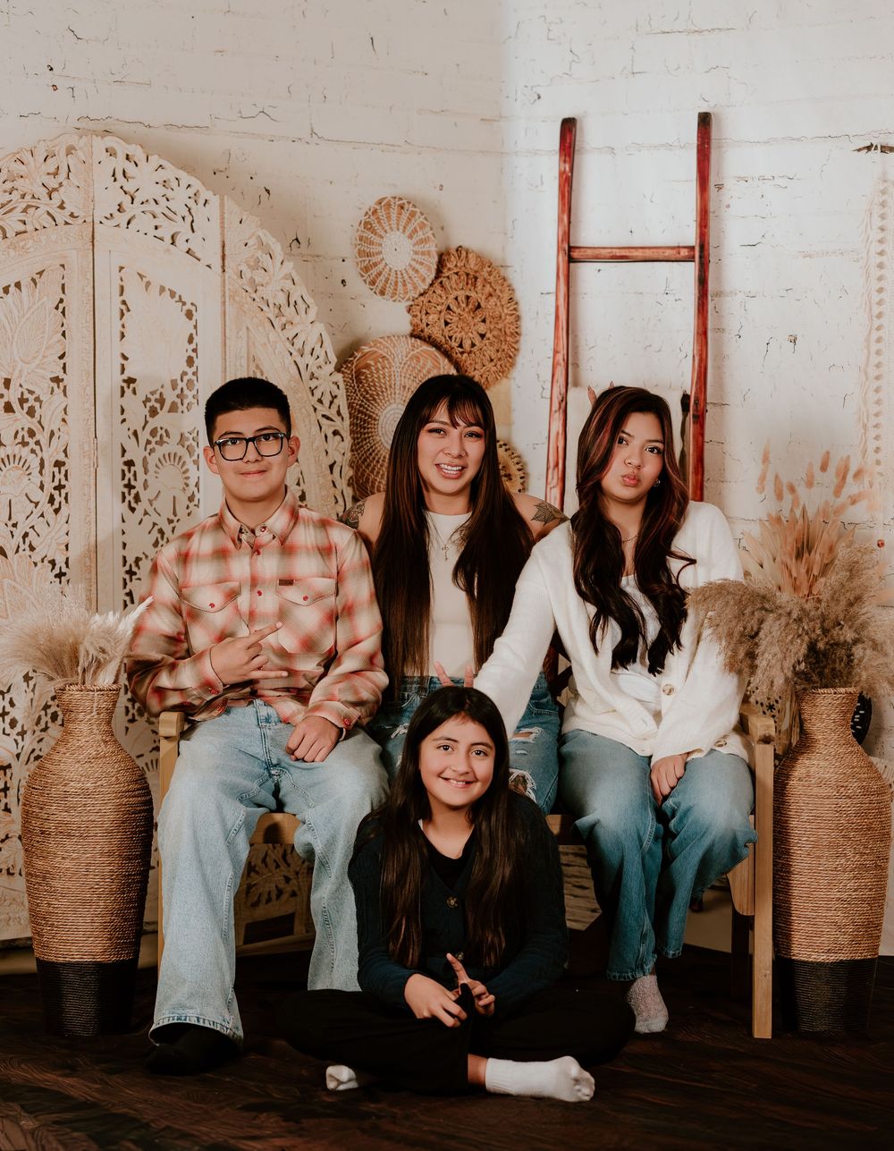A group sits casually on the floor against a beige wall decorated with woven baskets and dried pampas grass.