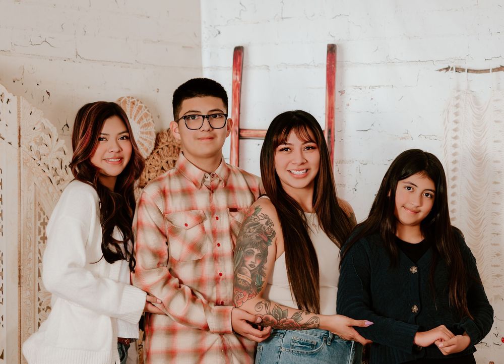 A group of friends pose together against a white wall in casual attire showing peace signs and smiles.