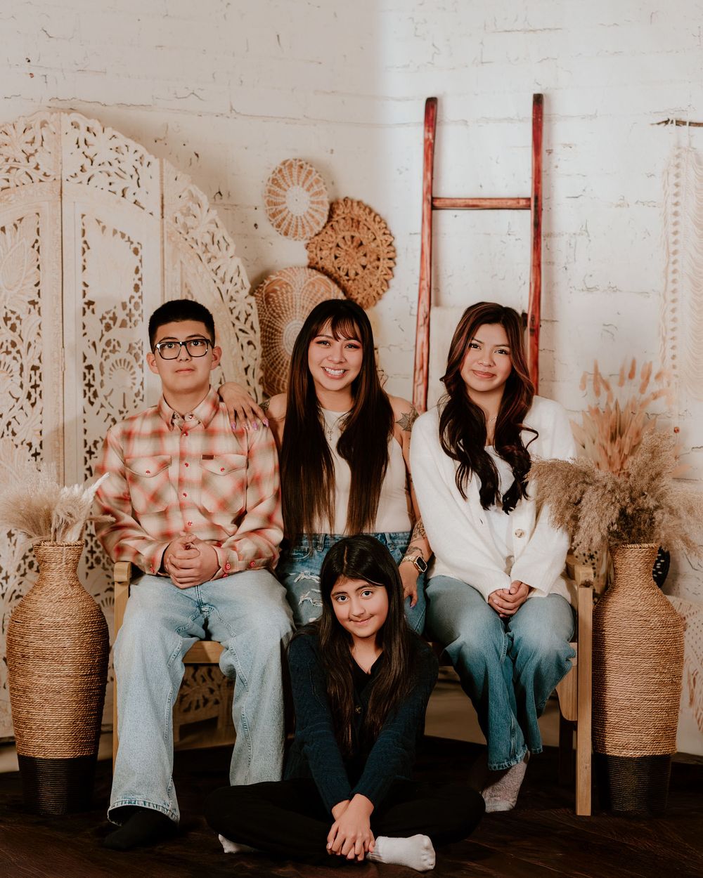 A group sits together in front of a rustic white backdrop with woven baskets and peacock chairs.